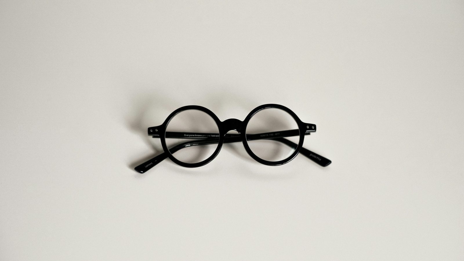 Illustrative round eyeglasses photographed on an ivory surface